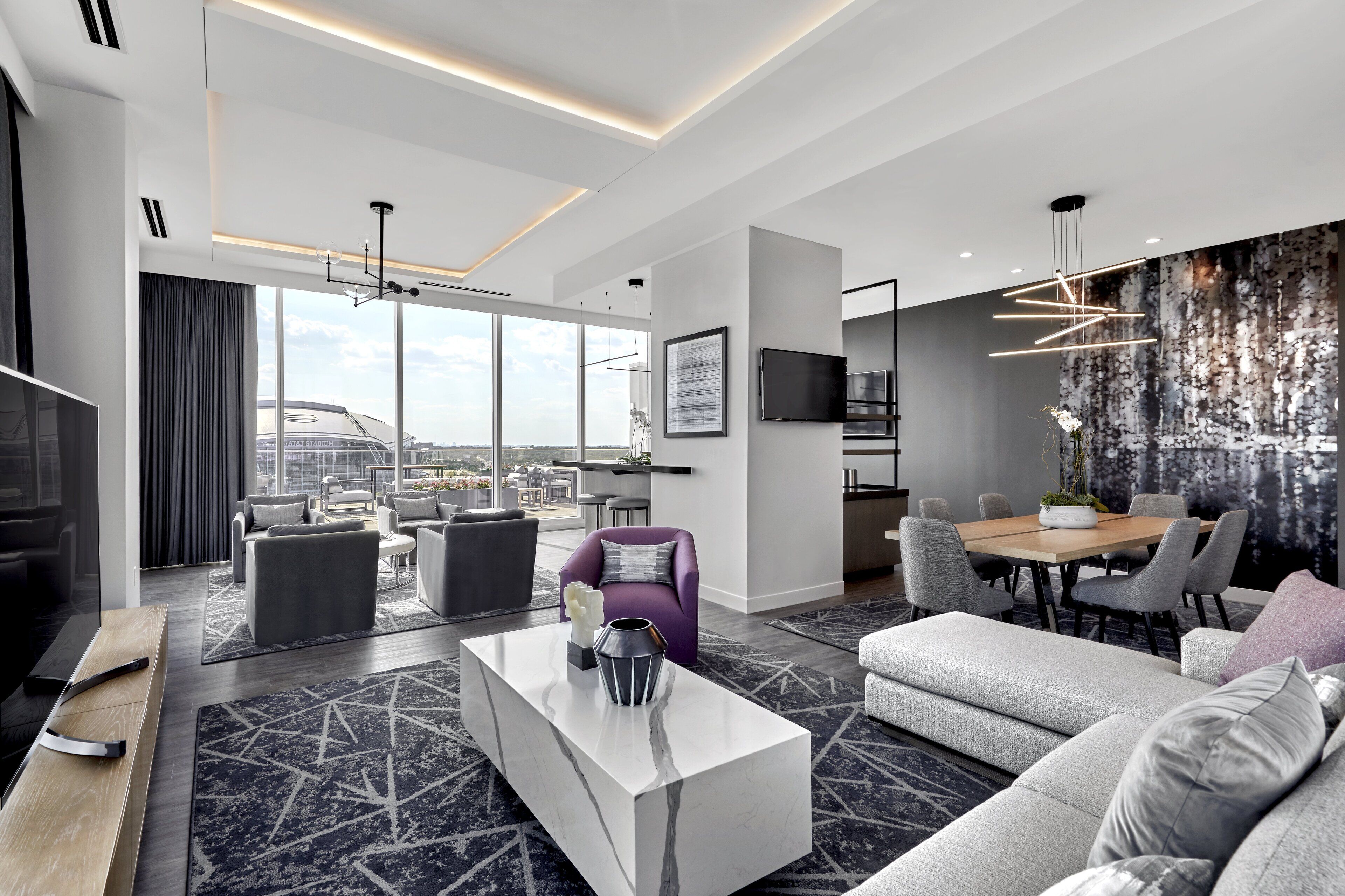 Et moderne hotelværelse med et stort vindue, et spiseområde og en siddeplads med sofaer og stole.