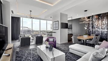 Et moderne hotelværelse med et stort vindue, et spiseområde og en siddeplads med sofaer og stole.
