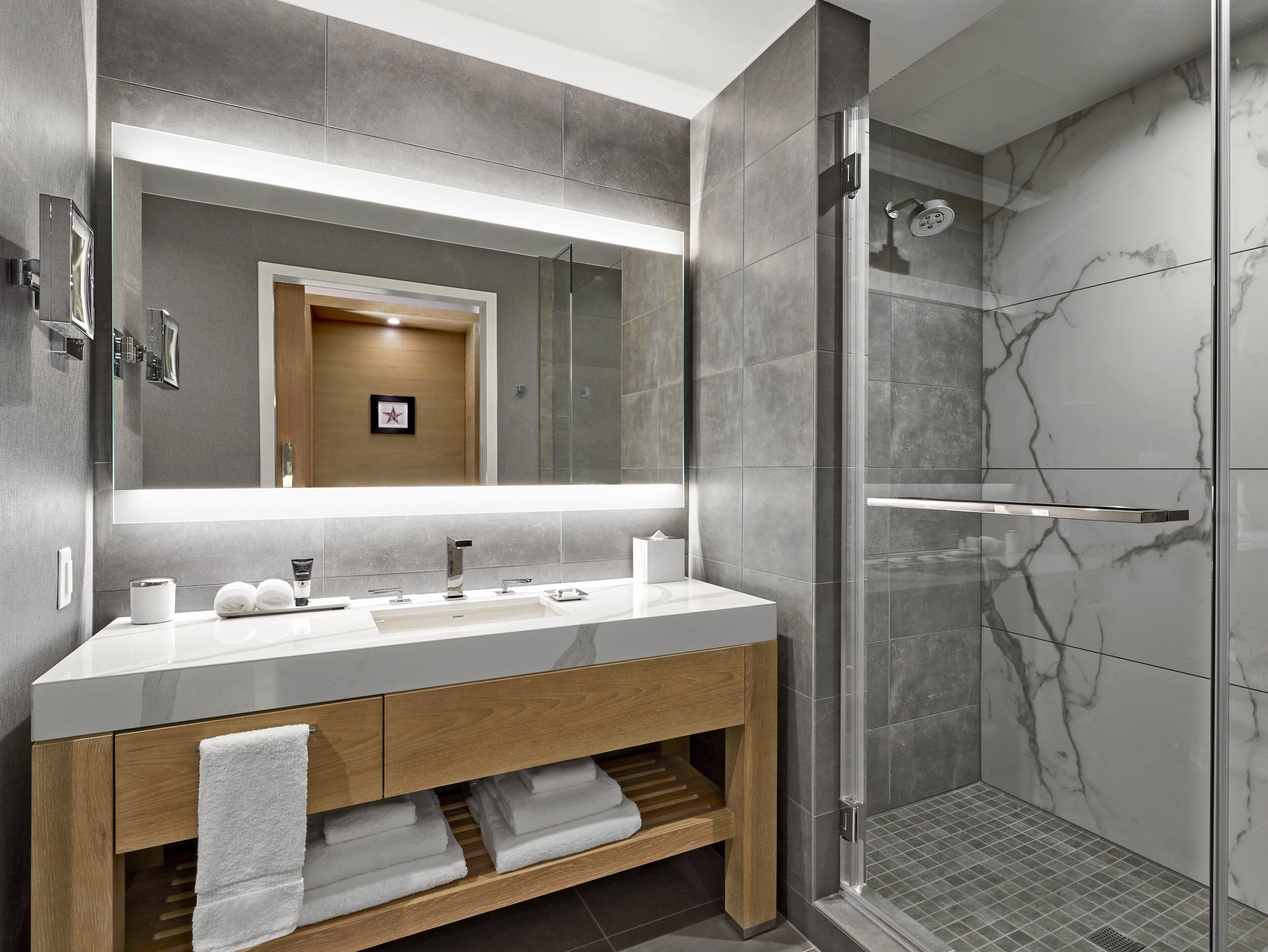 Une salle de bain moderne avec un grand miroir, une douche et un meuble-lavabo doté d’un évier et d’un porte-serviettes.