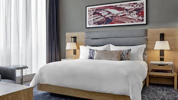 A modern hotel room with a large bed, two bedside tables with lamps, a headboard, and a large framed artwork above the bed.