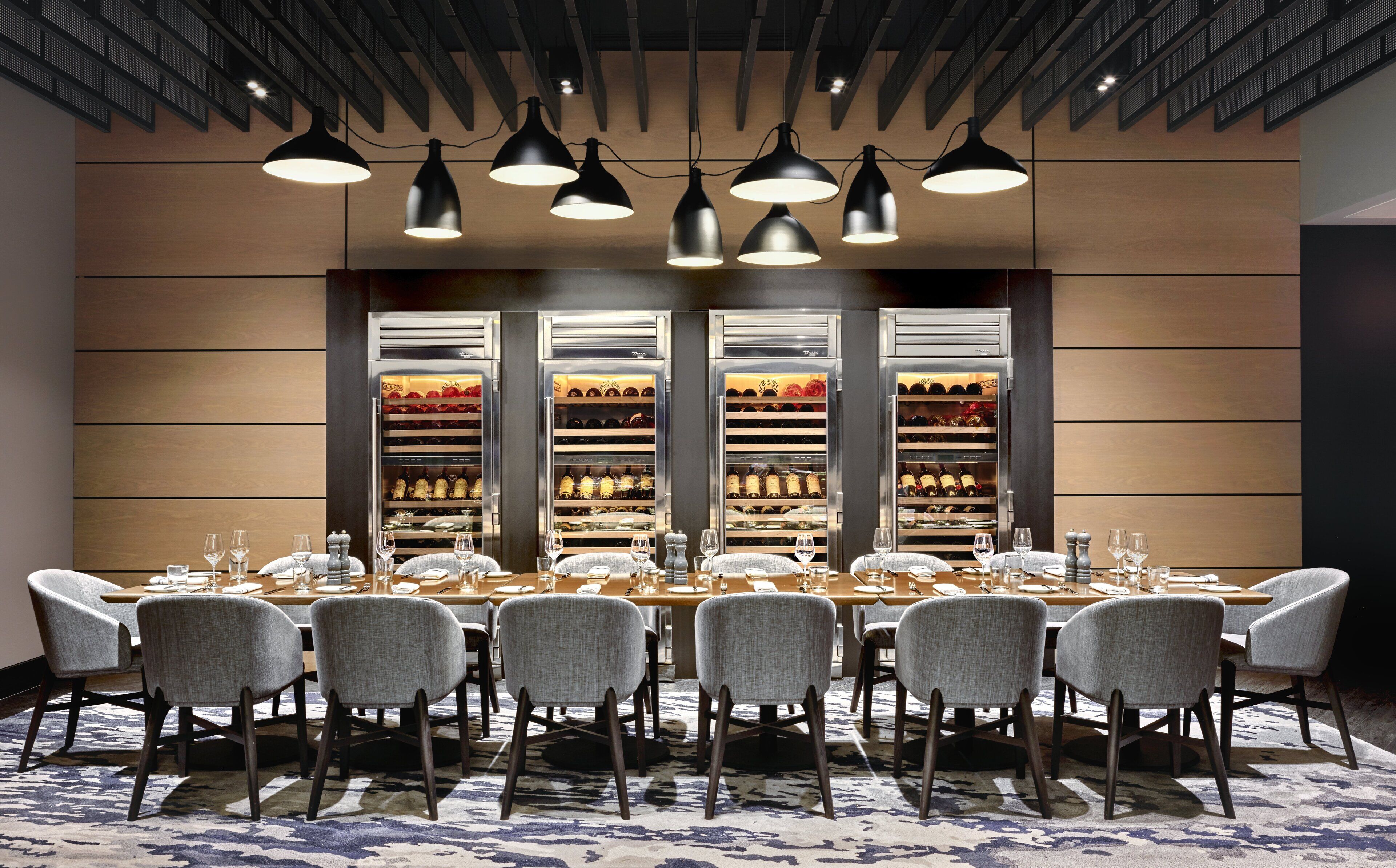 A conference room with a long table, multiple chairs, and a wine rack with bottles behind the table.