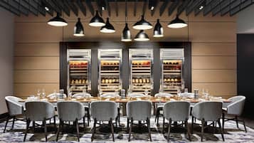 A conference room with a long table, multiple chairs, and a wine rack with bottles behind the table.