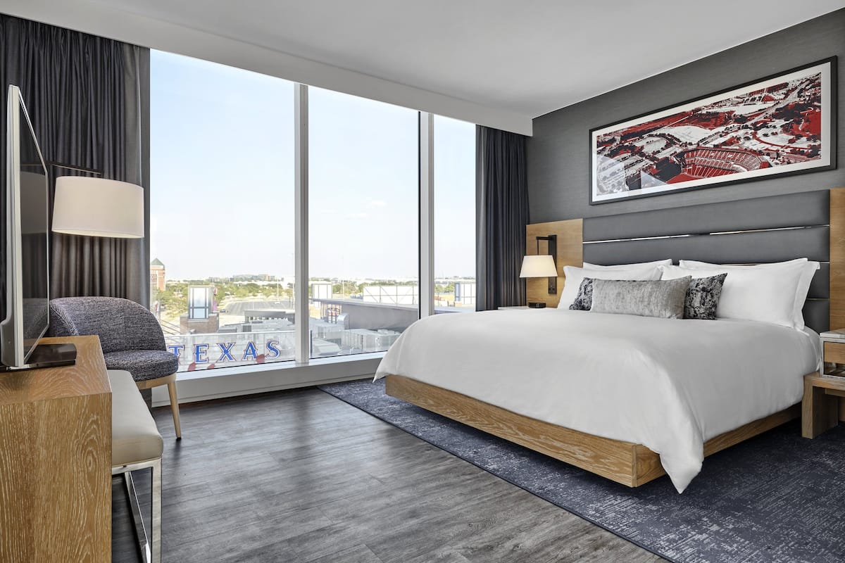 Moderni hotellihuone, jossa on suuri sänky, työpöytä, tuoli ja suuri ikkuna, josta avautuu näkymä kaupunkiin.
