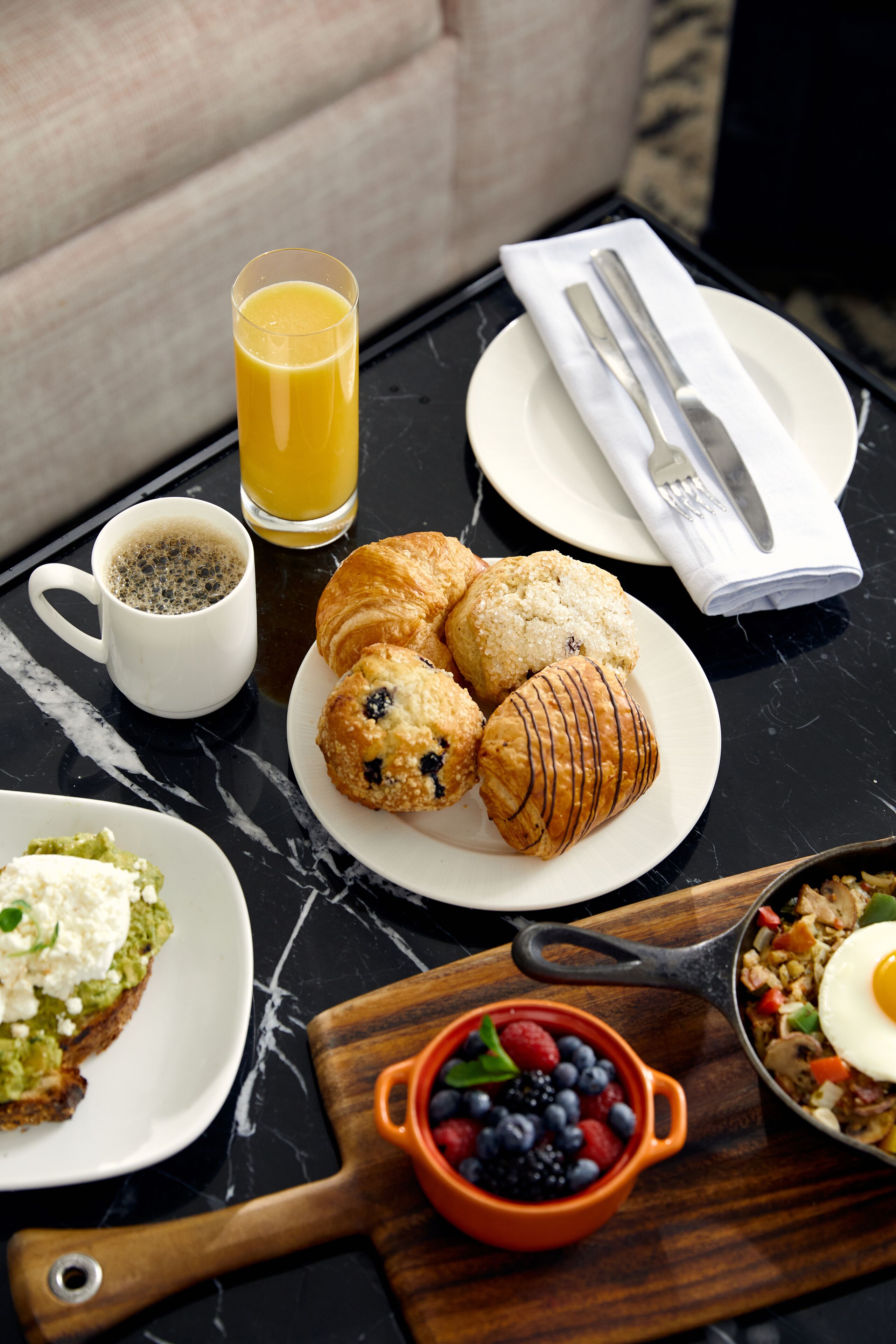 A breakfast table with croissants, a glass of orange juice, a cup of coffee, a plate of scrambled eggs, and a bowl of berries.