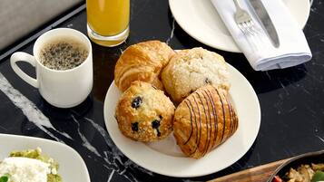 A breakfast table with croissants, a glass of orange juice, a cup of coffee, a plate of scrambled eggs, and a bowl of berries.