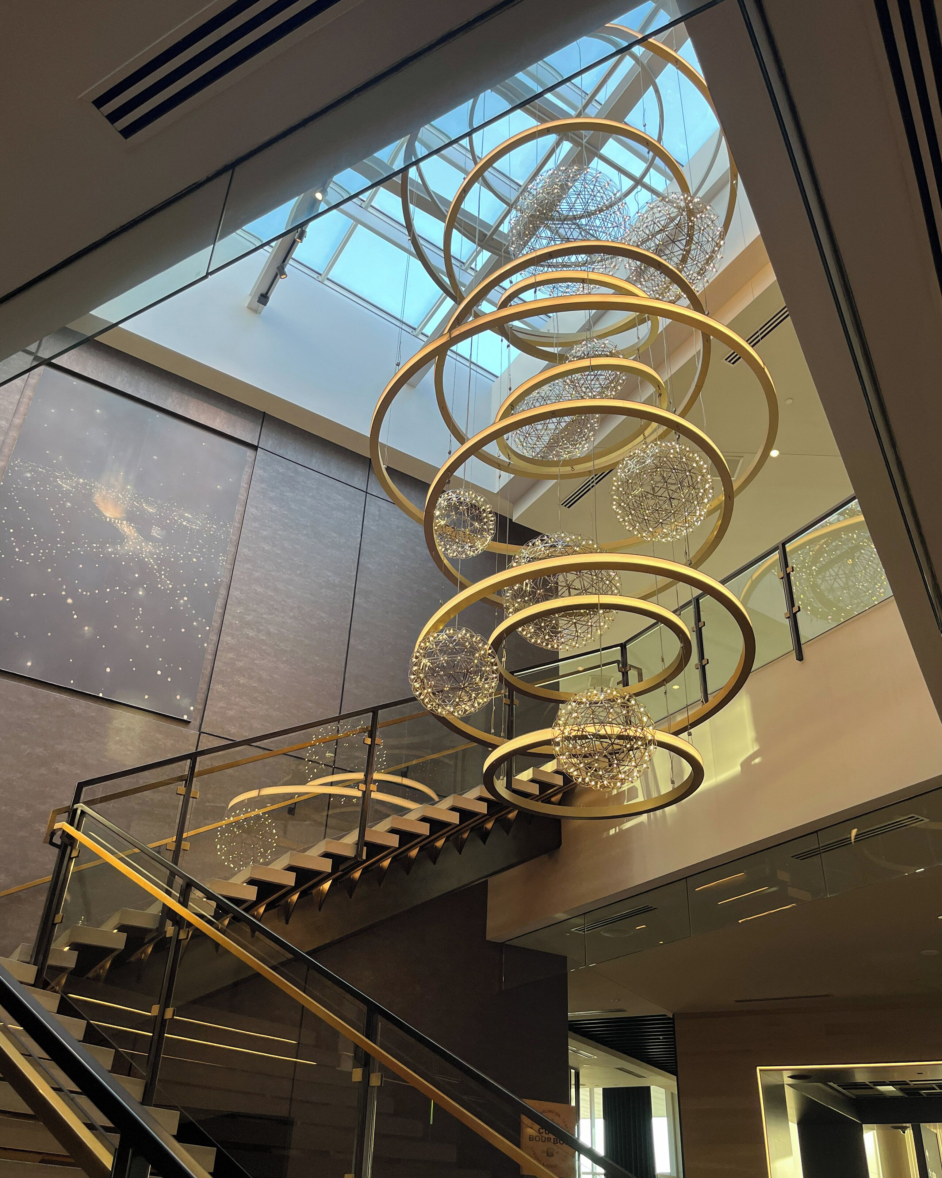 A modern interior with a spiral staircase, glass railings, and a geometric chandelier.