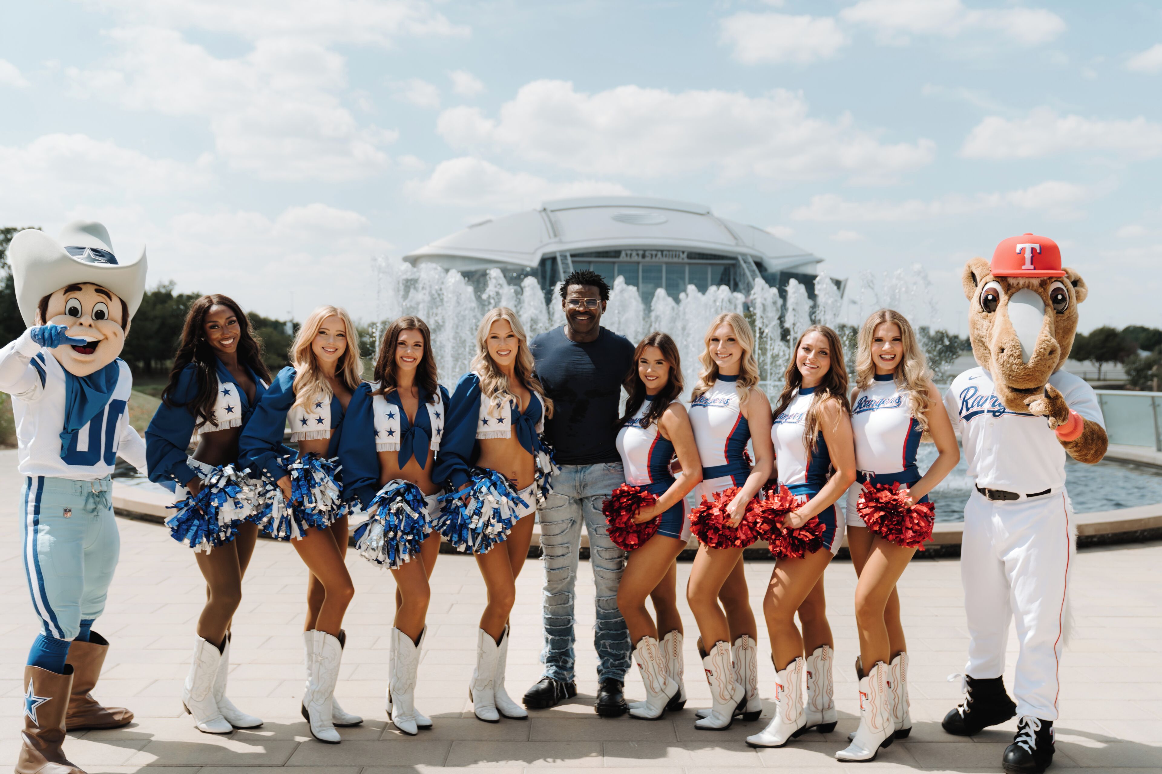 A group of cheerleaders and mascots in front of a stadium with a fountain.