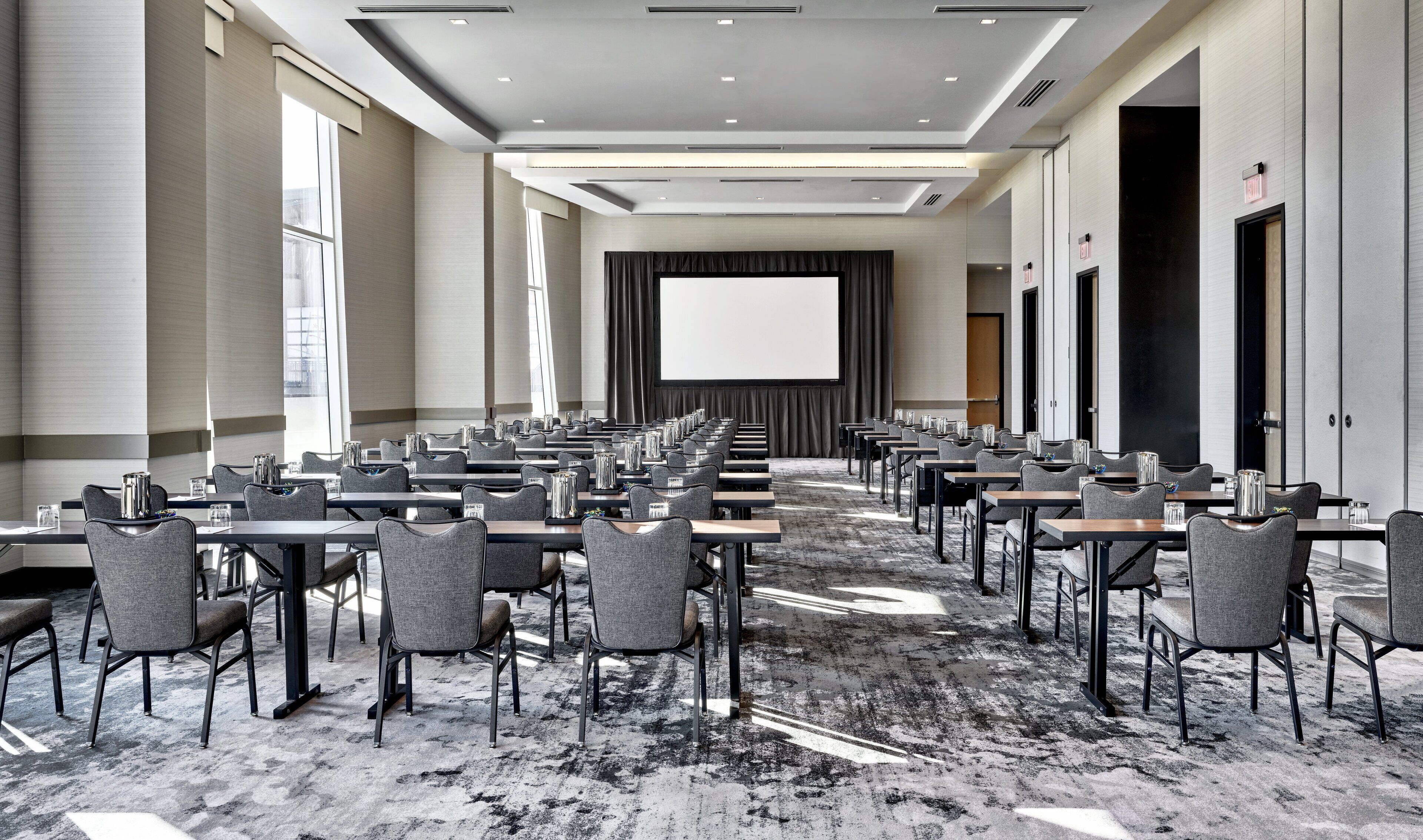 Une salle de conférence avec des rangées de tables et de chaises, un grand écran à l’avant et un sol recouvert de moquette.