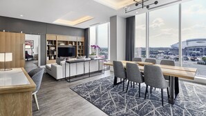 Habitació d'hotel moderna amb zona de dinar, un sofà, televisió i un gran finestral amb vista a la ciutat.