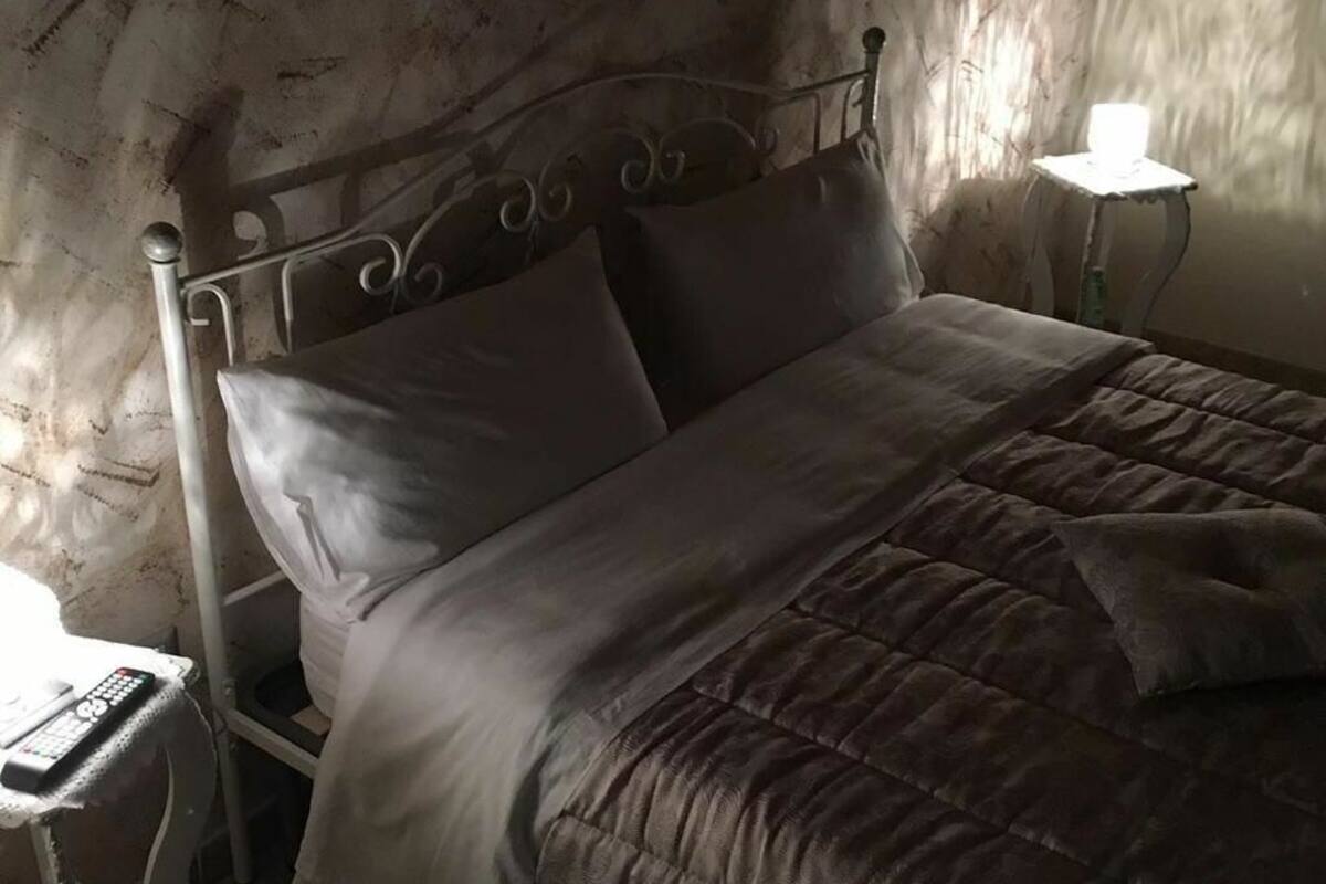 A bed with a metal headboard, a bedside table with a lamp, and a wall with a textured pattern.