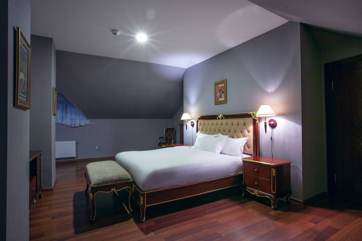 Une chambre à coucher avec un grand lit, des lampes de chevet, une table de chevet en bois, un banc et un radiateur.