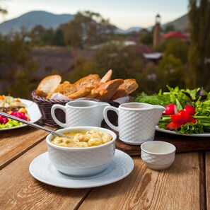 A table with a bowl of soup, two white cups, a basket of bread, and a plate with vegetables. - Sheki Palace Hotel (Sheki)