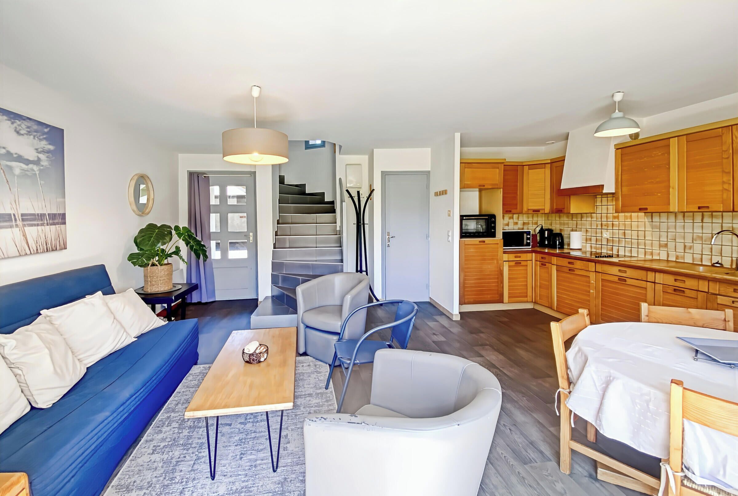 Una sala de estar moderna con un sofá, sillones, una mesa de centro y una escalera que lleva a una cocina.