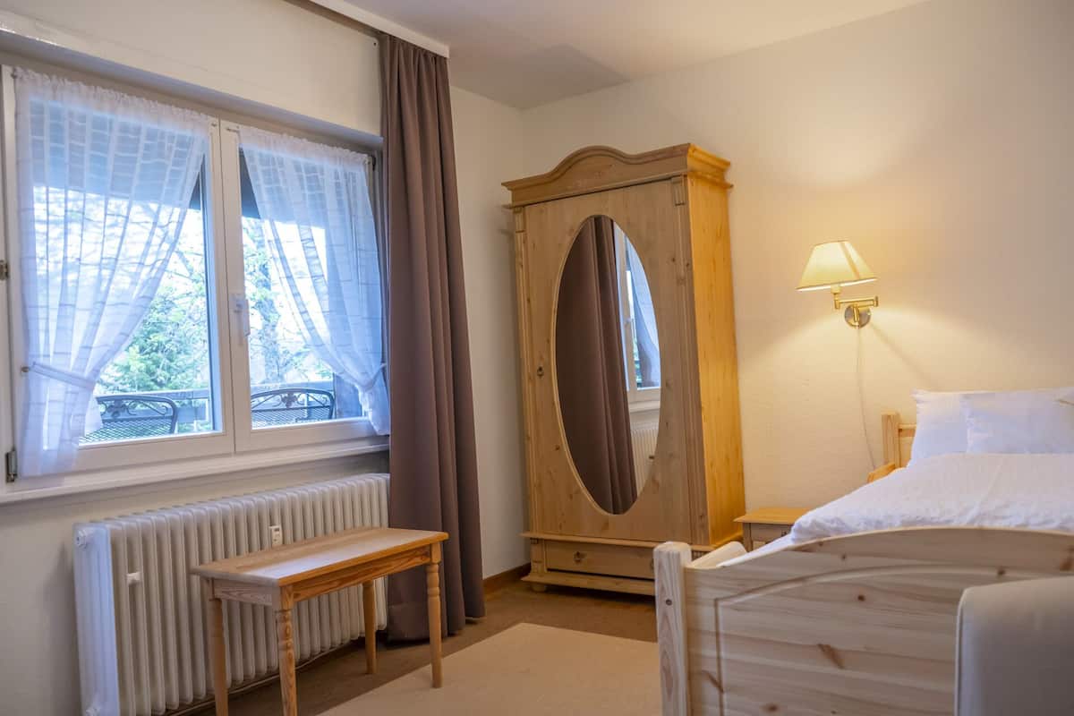 Ein Schlafzimmer mit Bett, einem Holzschrank, einem Tisch, einem Heizkörper und einem Fenster mit Vorhängen.