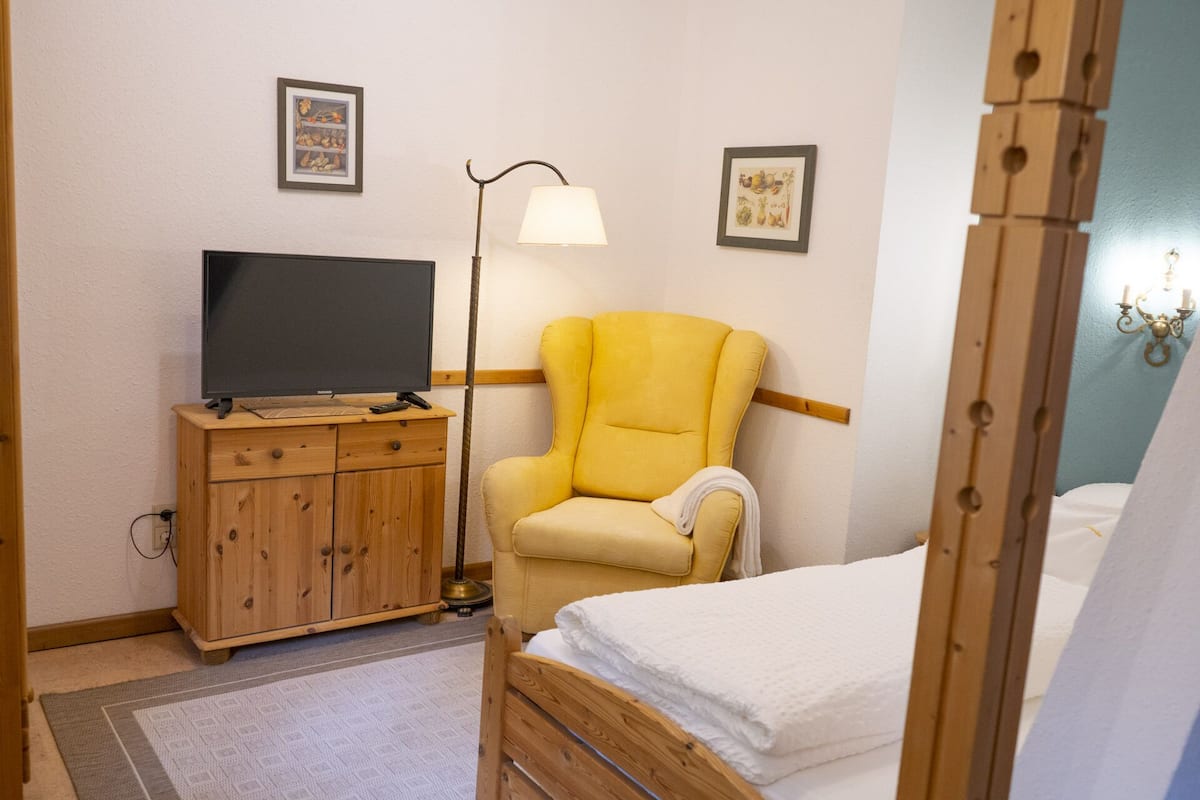 Ein Schlafzimmer mit einem Bett, einem Holzschrank mit Fernseher, einem gelben Sessel und einer Stehlampe.