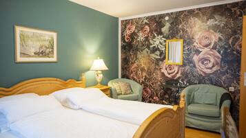 A bedroom with a bed, a nightstand, a lamp, a chair, and a floral wallpaper.