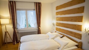 A bedroom with a wooden headboard, a bed with white linens, a standing lamp, and a window with curtains. - NATURION Hotel Hinterzarten (Hinterzarten)