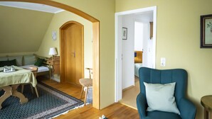 A room with a bed, a table with a lamp, a chair, and a blue armchair. - NATURION Hotel Hinterzarten (Hinterzarten)