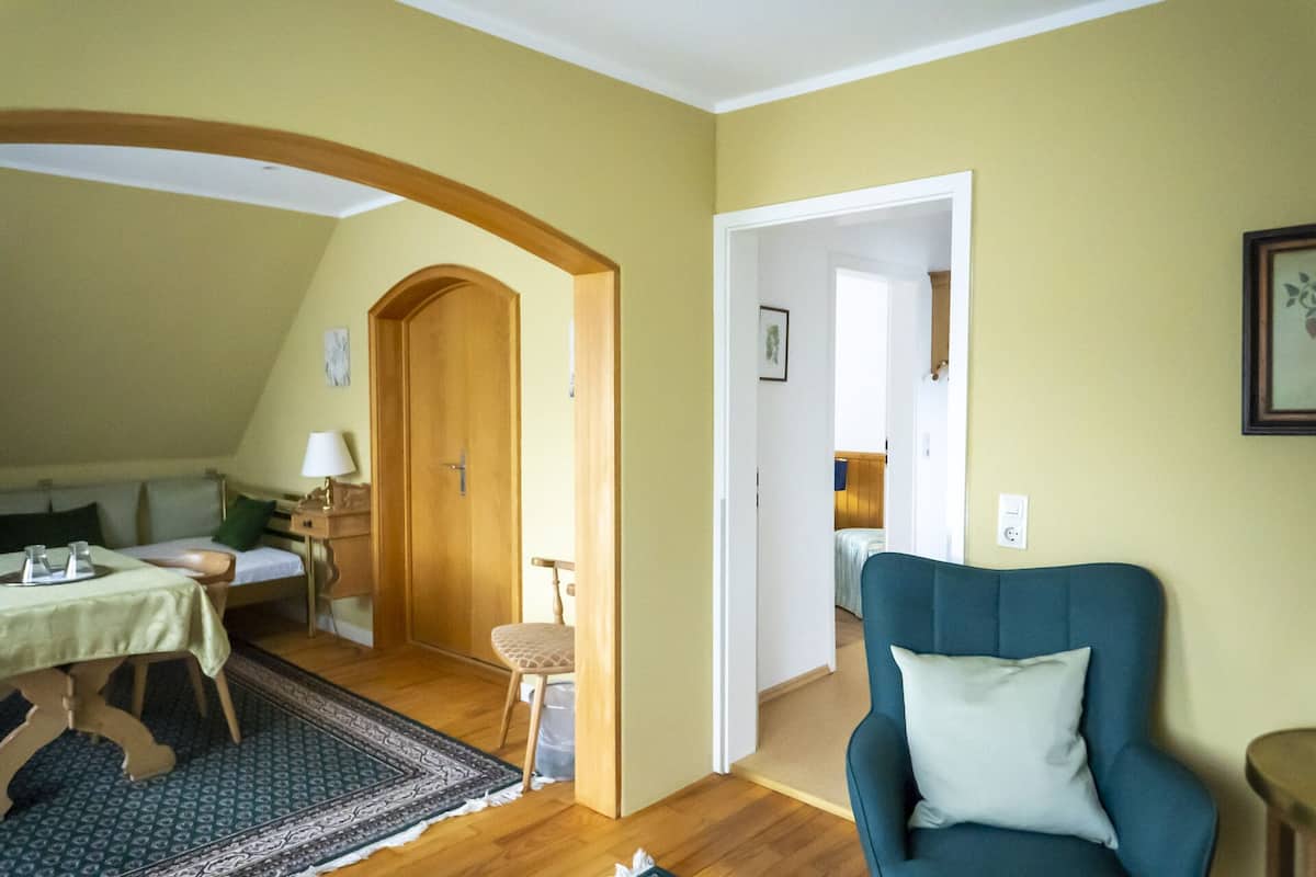 Ein Zimmer mit einem Bett, einem Tisch mit Lampe, einem Stuhl und einem blauen Sessel.
