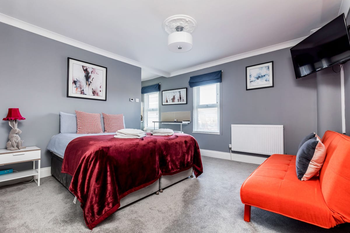 A bedroom with a bed, a red sofa, a white bedside table, and a red lamp.