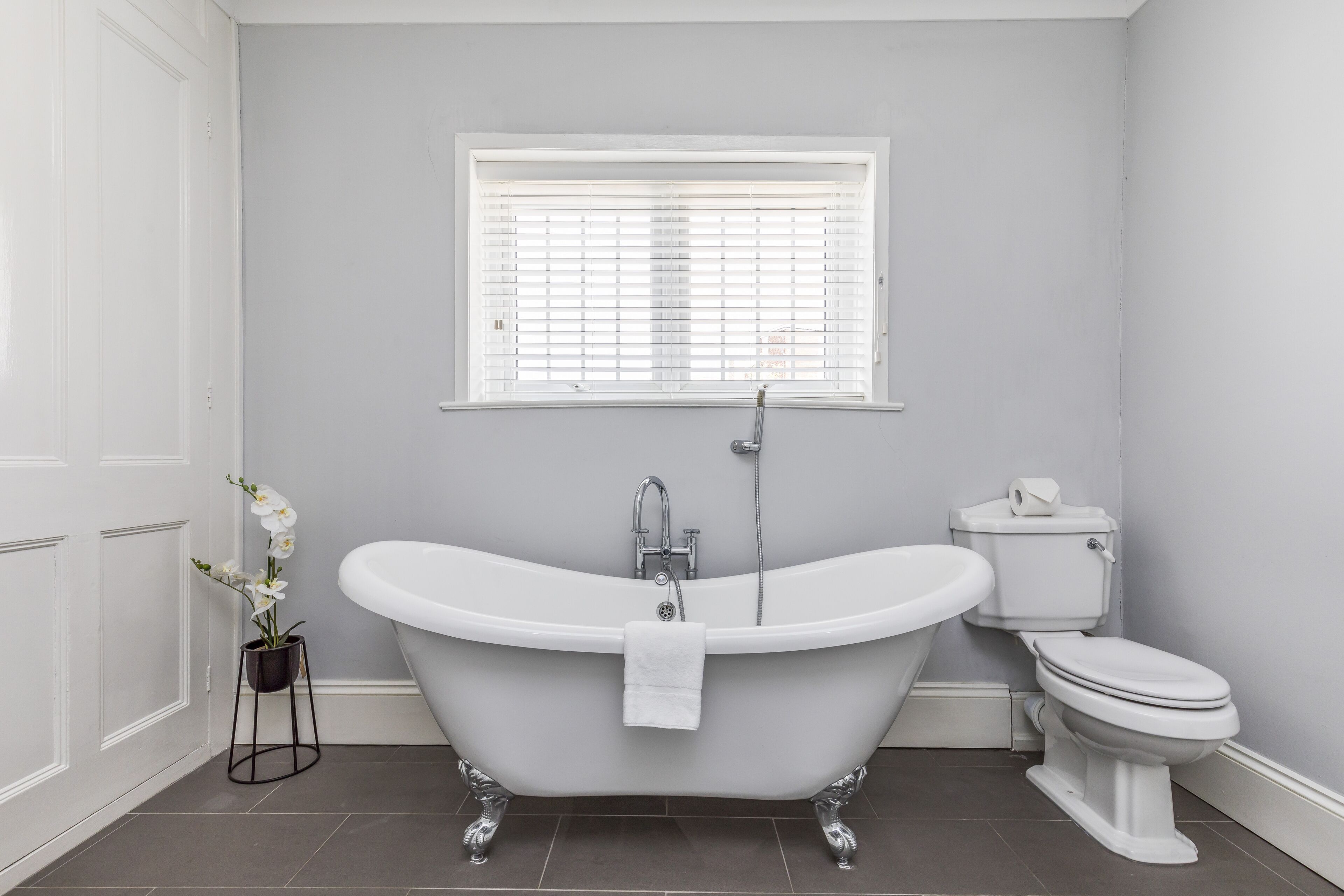 A bathroom with a freestanding bathtub, a toilet, and a window with blinds.