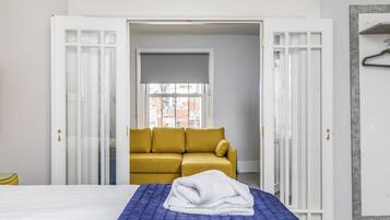Habitación de hotel con cama, sofá amarillo y ventana con vistas a edificios.