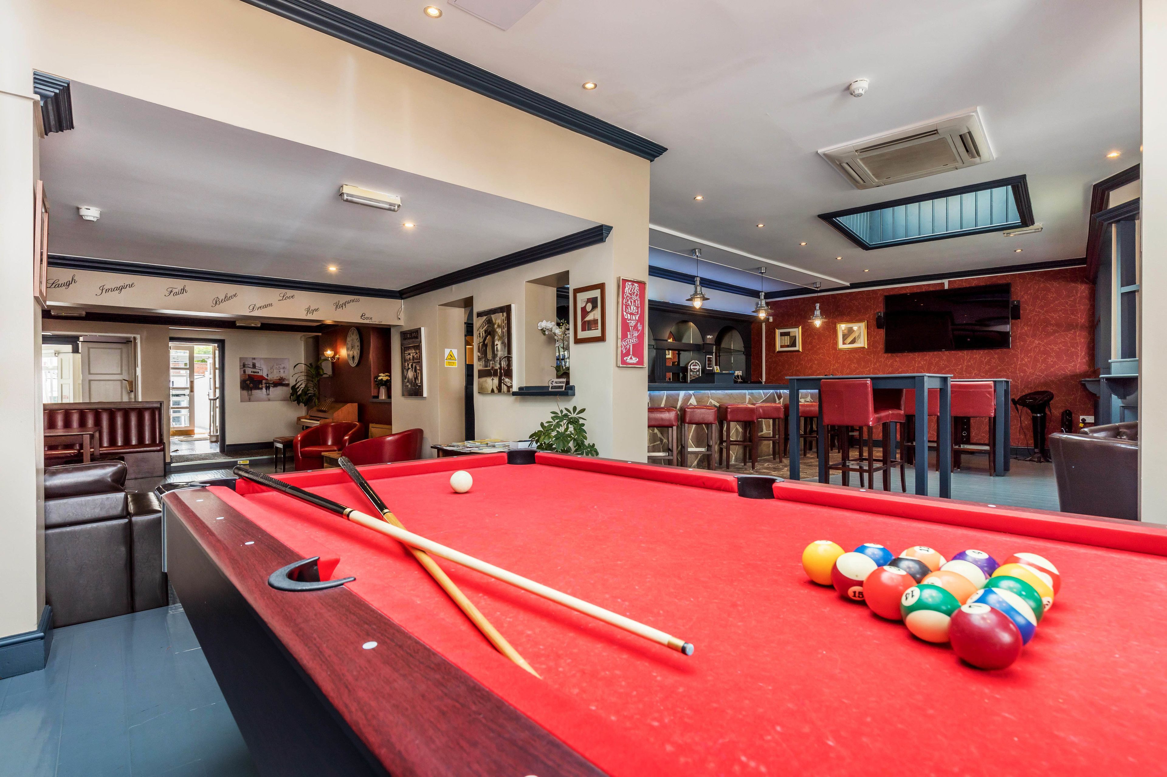 A pool table with balls and cues, a bar area with stools, and a seating area with a red couch.
