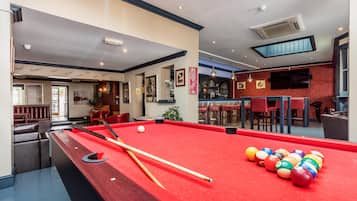 A pool table with balls and cues, a bar area with stools, and a seating area with a red couch.
