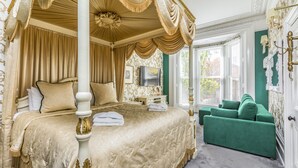 A luxurious bedroom with a four-poster bed, a green sofa, and a large window providing natural light. - Ashbys (Portsmouth)