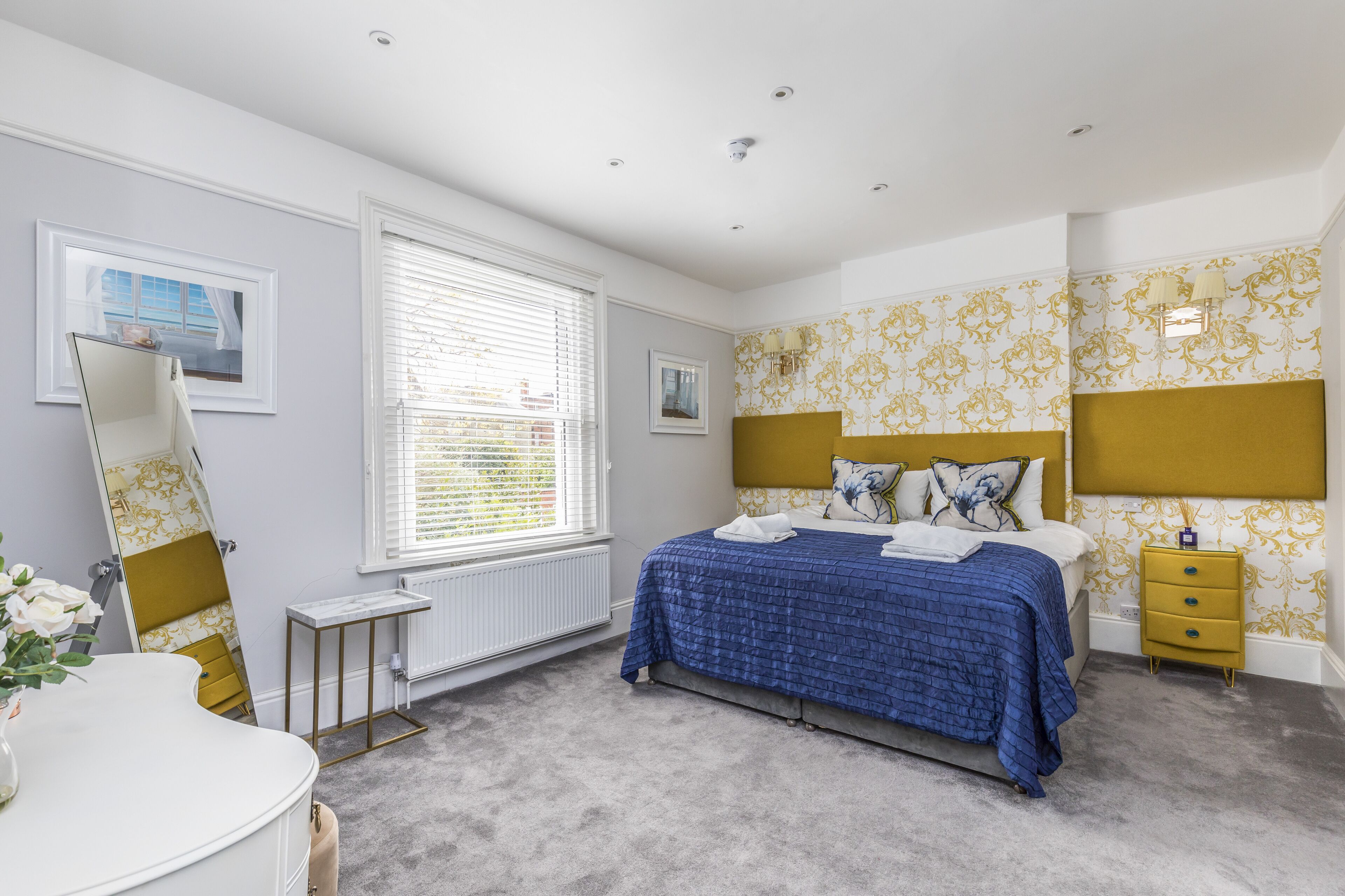 A bedroom with a bed, bedside table, dresser, and a window with blinds.