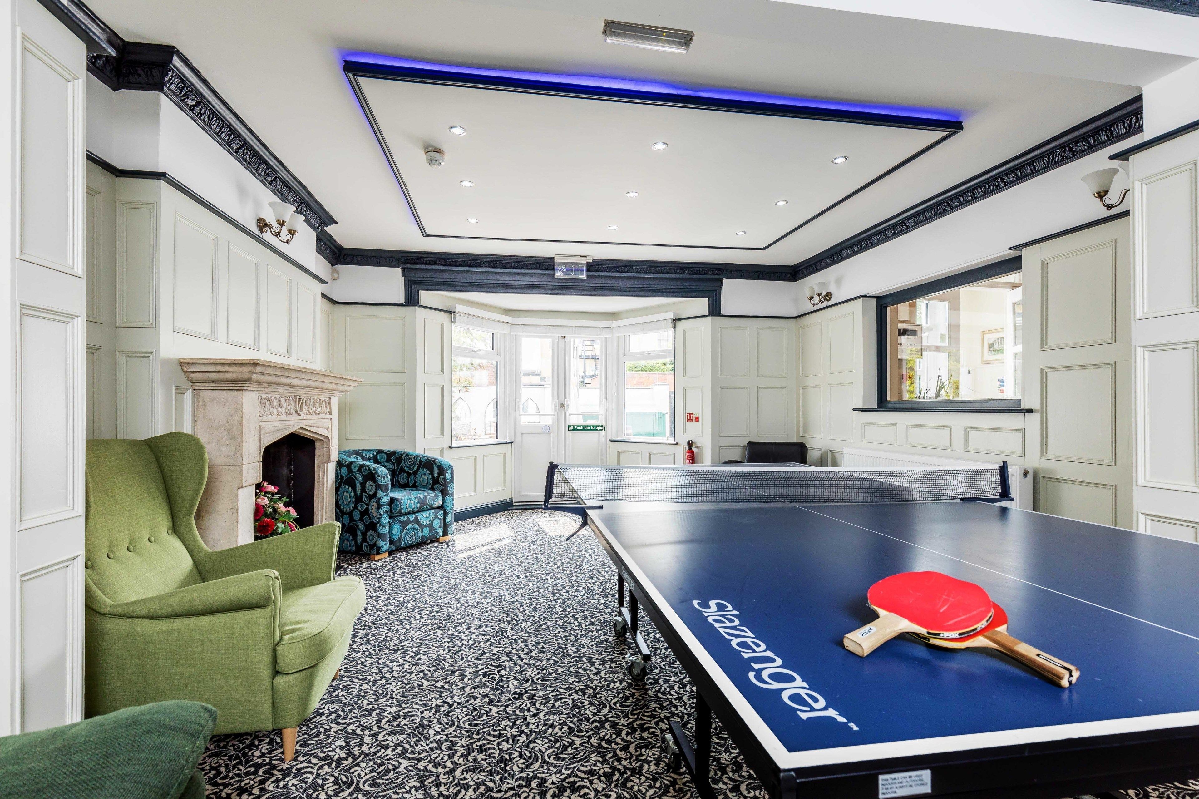 Una habitación con mesa de ping pong, sillones verdes y suelo estampado.