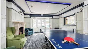 Una habitación con mesa de ping pong, sillones verdes y suelo estampado.