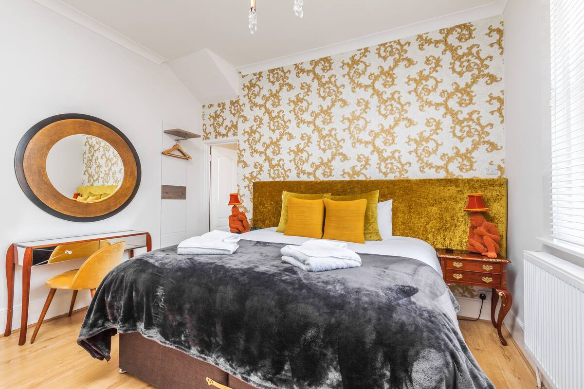 A bedroom with a large bed, a round mirror, a chair, and a dresser.