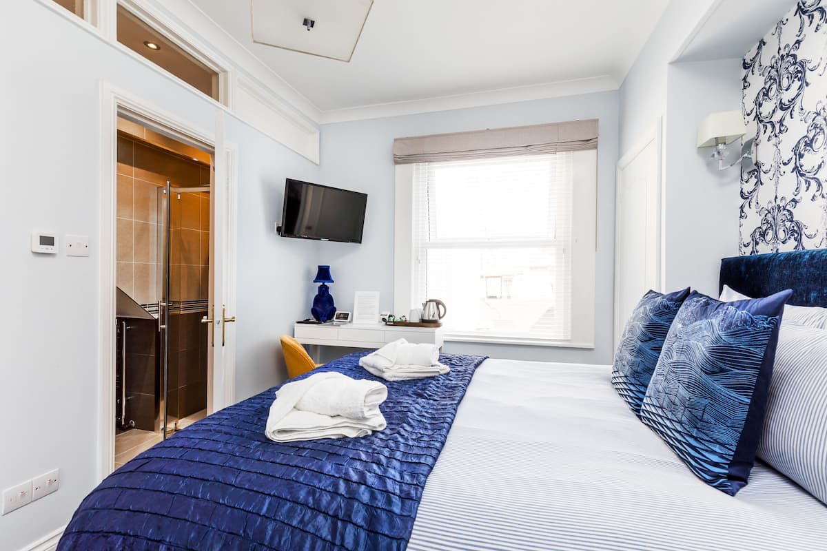 A hotel room with a bed, a desk, a TV, and a window.