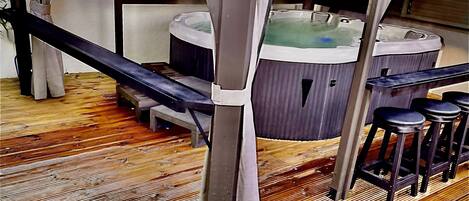 Een houten terras met een jacuzzi, barstoelen en een kleine waterpartij.