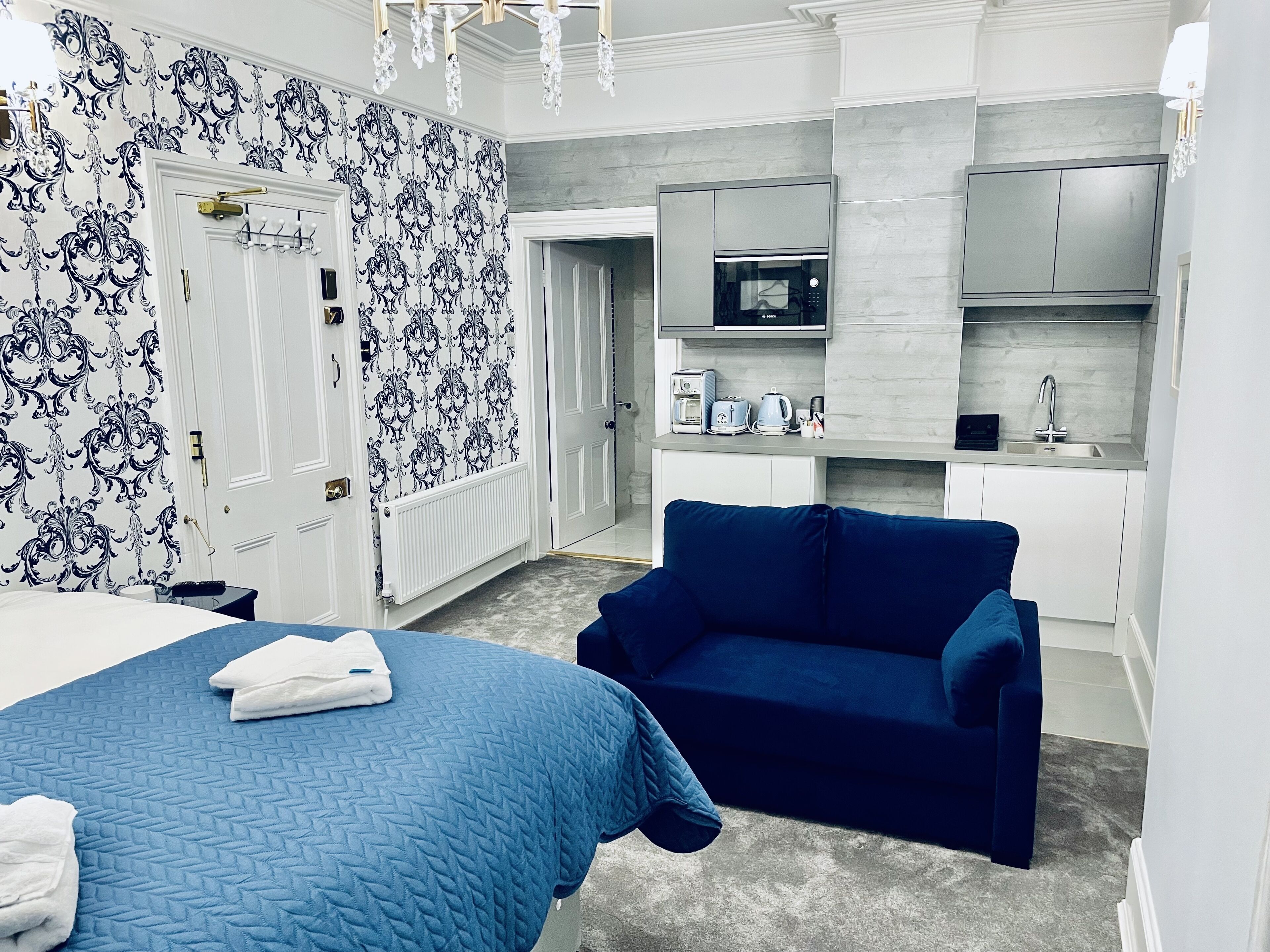 Ein Hotelzimmer mit einem Bett, einem blauen Sofa, einer Küchenzeile mit Mikrowelle und Toaster sowie einem gemusterten Wandteppich.
