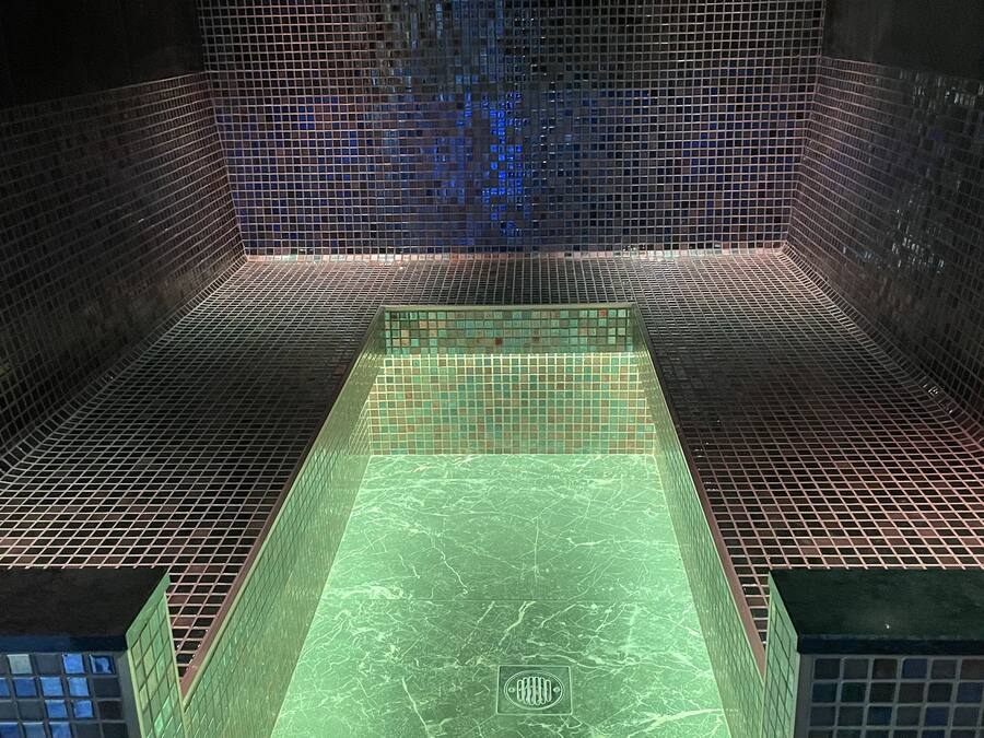 Ein rechteckiger Pool mit grün-marmorierter Bodenfläche, umgeben von dunklen Mosaikfliesen.