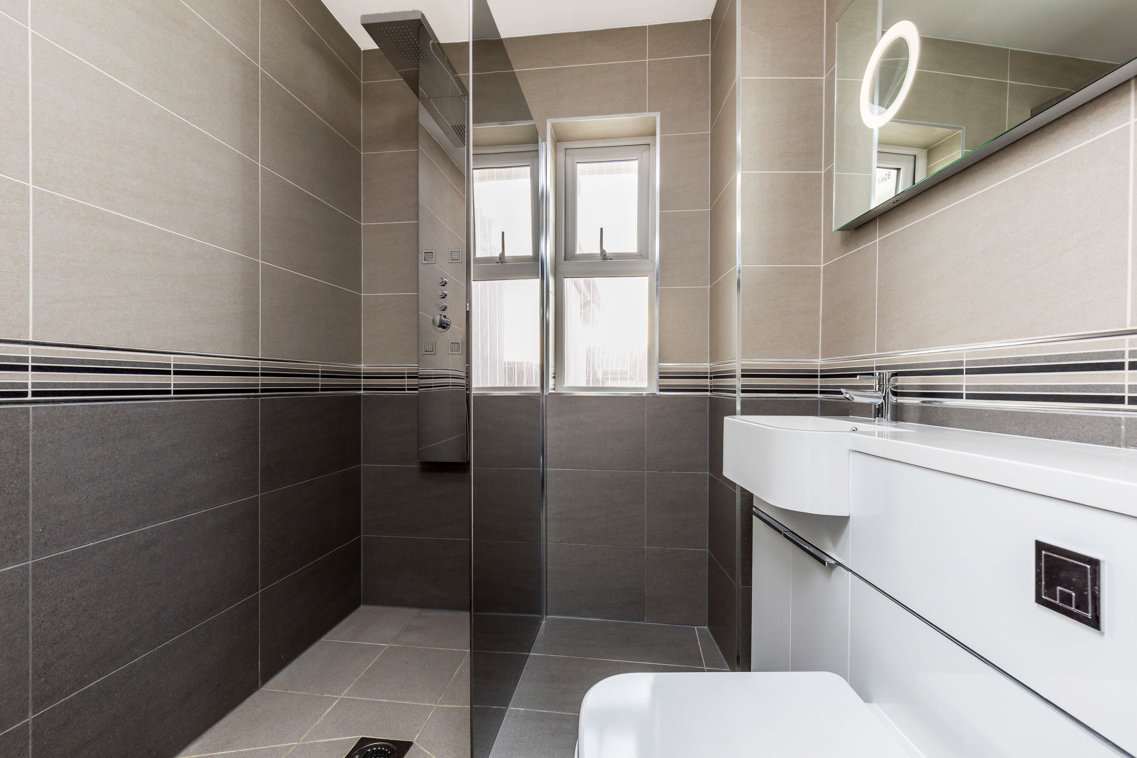 Ein modernes Badezimmer mit Duschkabine aus Glas, einem weißen Waschbecken und einem Spiegel mit Beleuchtung.