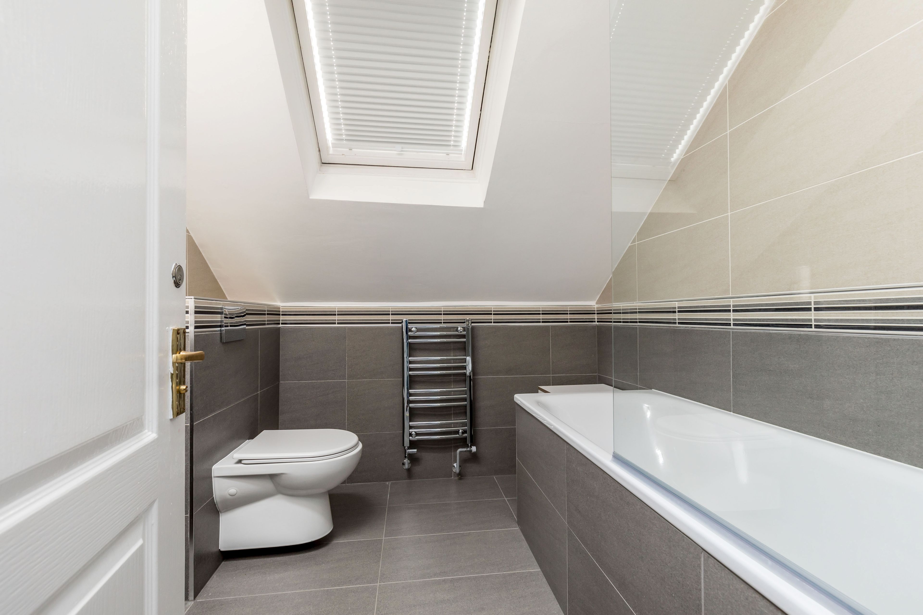A modern bathroom with a skylight, a toilet, a bathtub, and a towel rack.