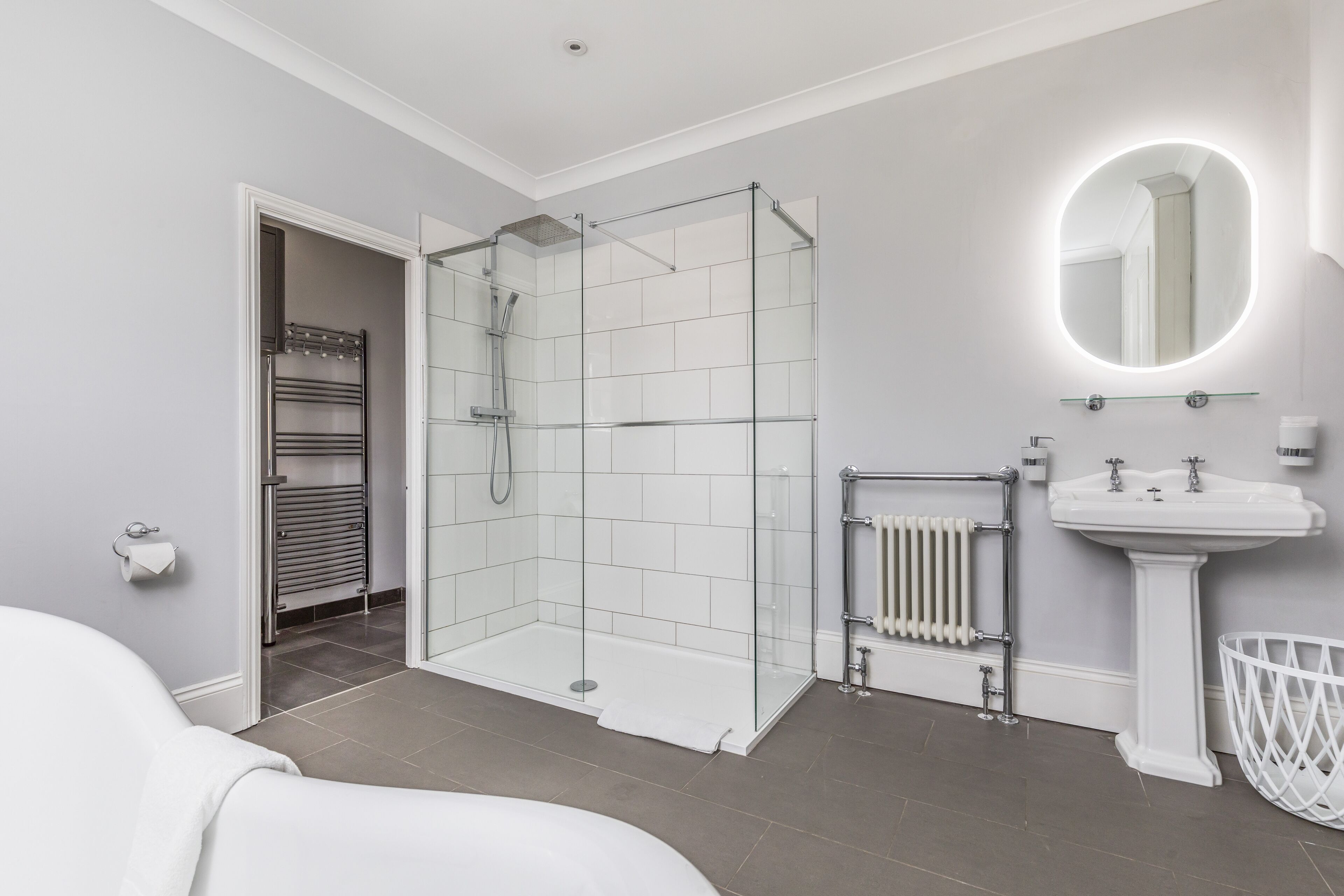A modern bathroom with a glass-enclosed shower, a pedestal sink, and a large mirror with integrated lighting.