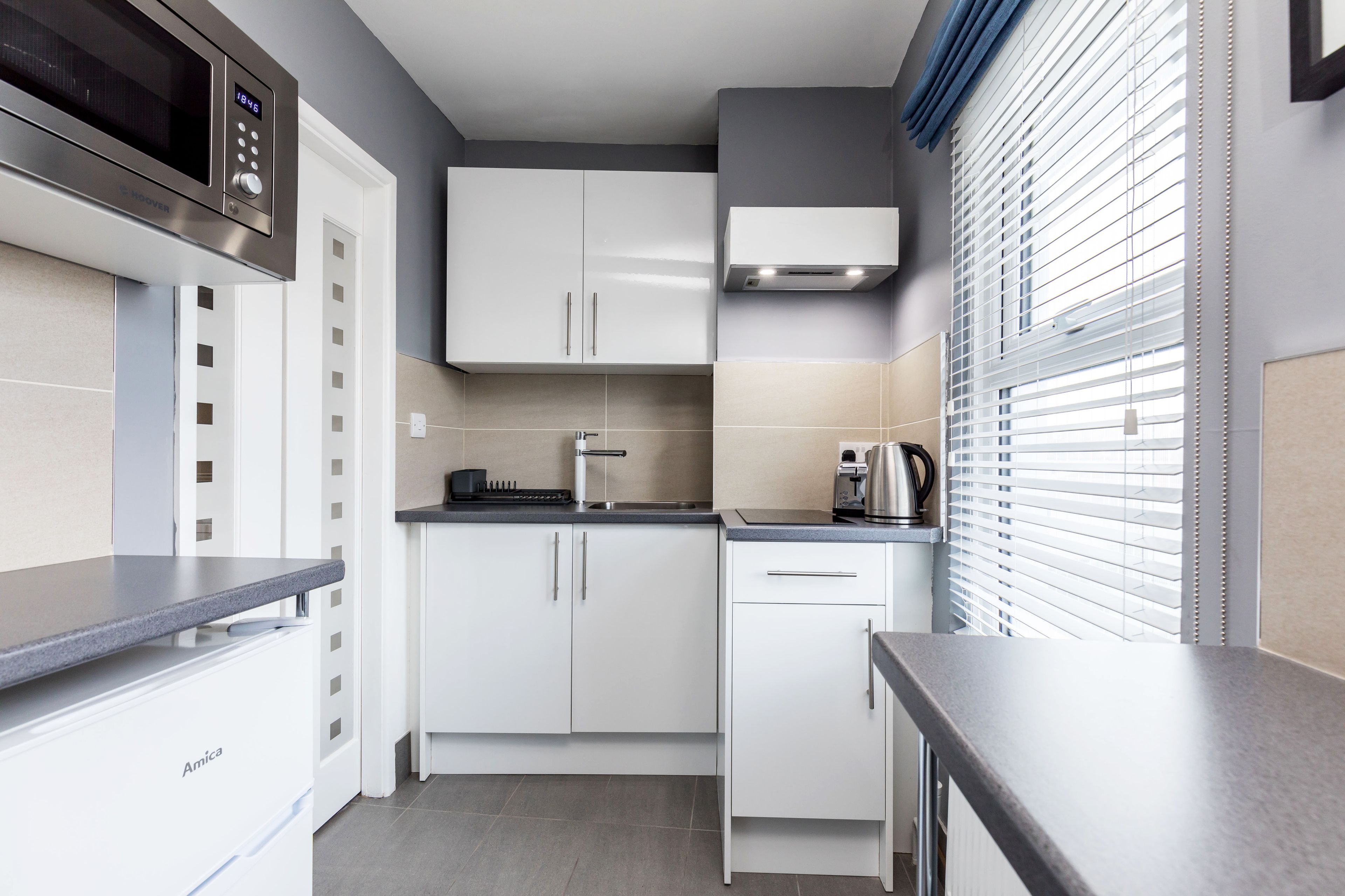 A compact kitchen with white cabinets, a built-in microwave, a kettle, and a coffee maker.