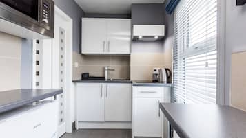 A compact kitchen with white cabinets, a built-in microwave, a kettle, and a coffee maker.
