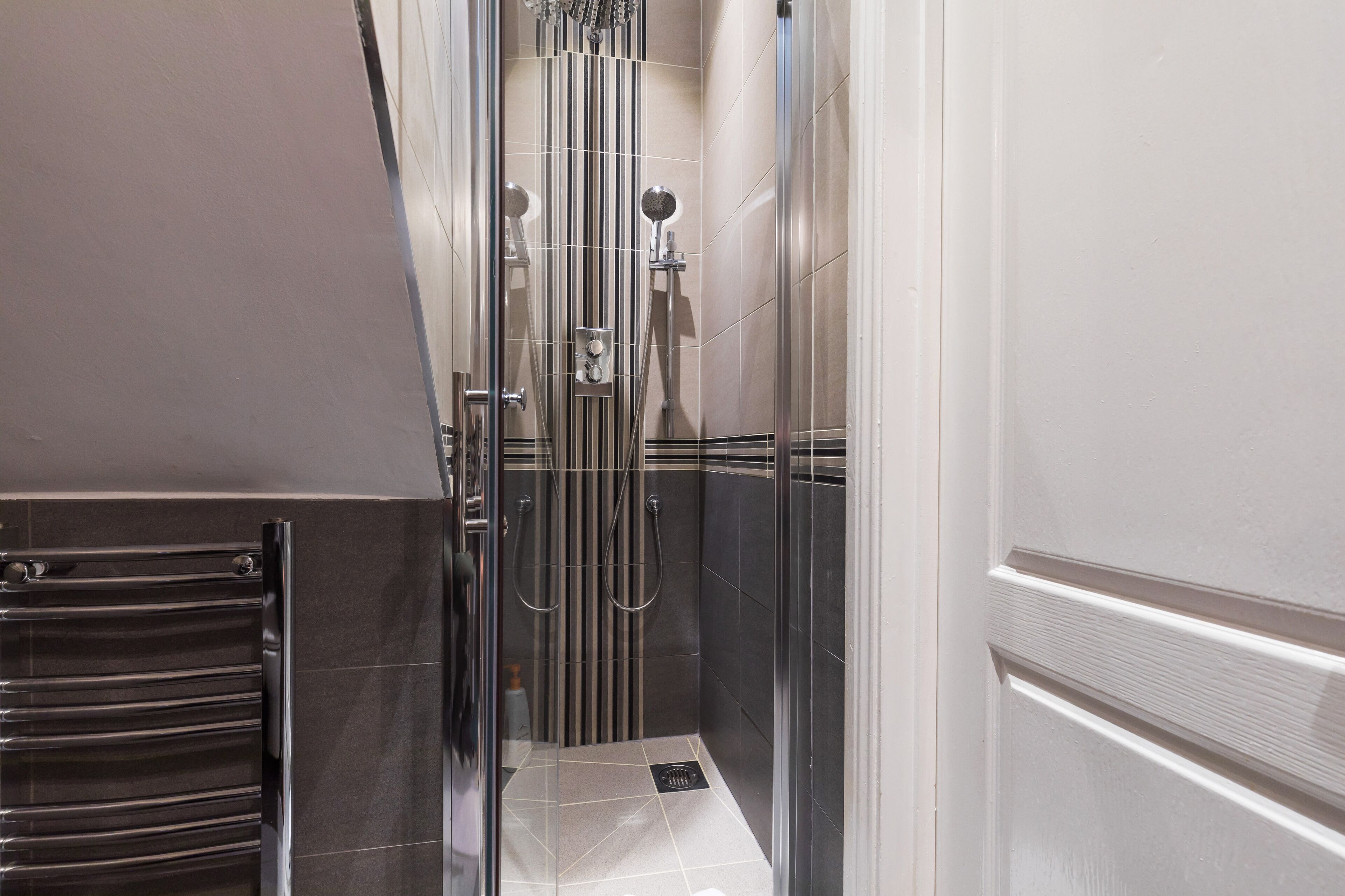 A modern bathroom with a glass shower enclosure, a stainless steel towel rack, and a tiled floor.