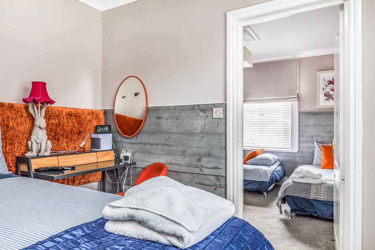 A modern bedroom with a bed, a desk, a chair, and a mirror.