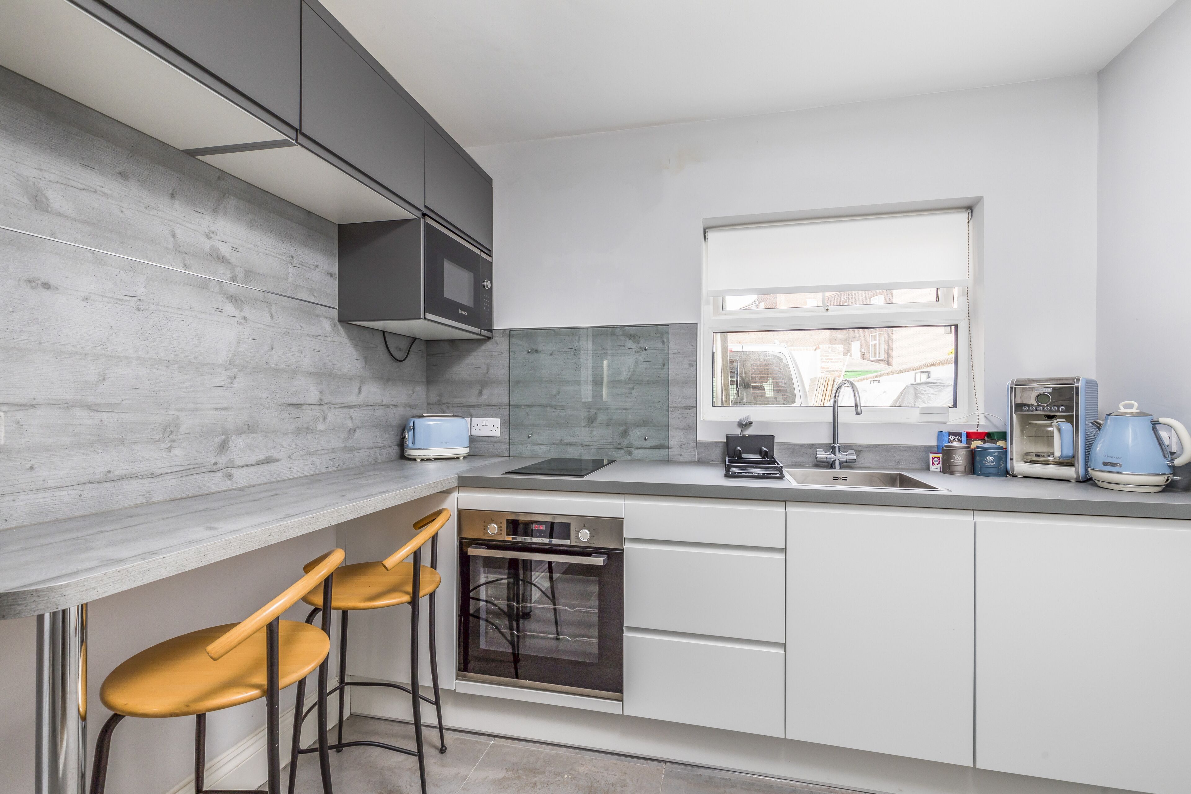 Una cocina moderna con microondas, horno y lavamanos integrados. Hay dos taburetes de bar y una ventana que ofrece vistas al exterior.