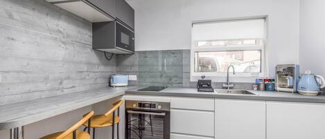 Una cocina moderna con microondas, horno y lavamanos integrados. Hay dos taburetes de bar y una ventana que ofrece vistas al exterior.