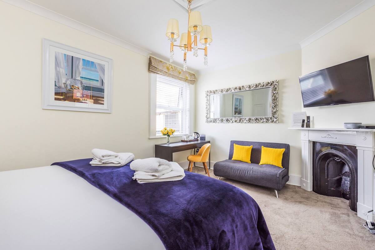 A hotel room with a bed, a desk, a sofa, a TV, and a fireplace.