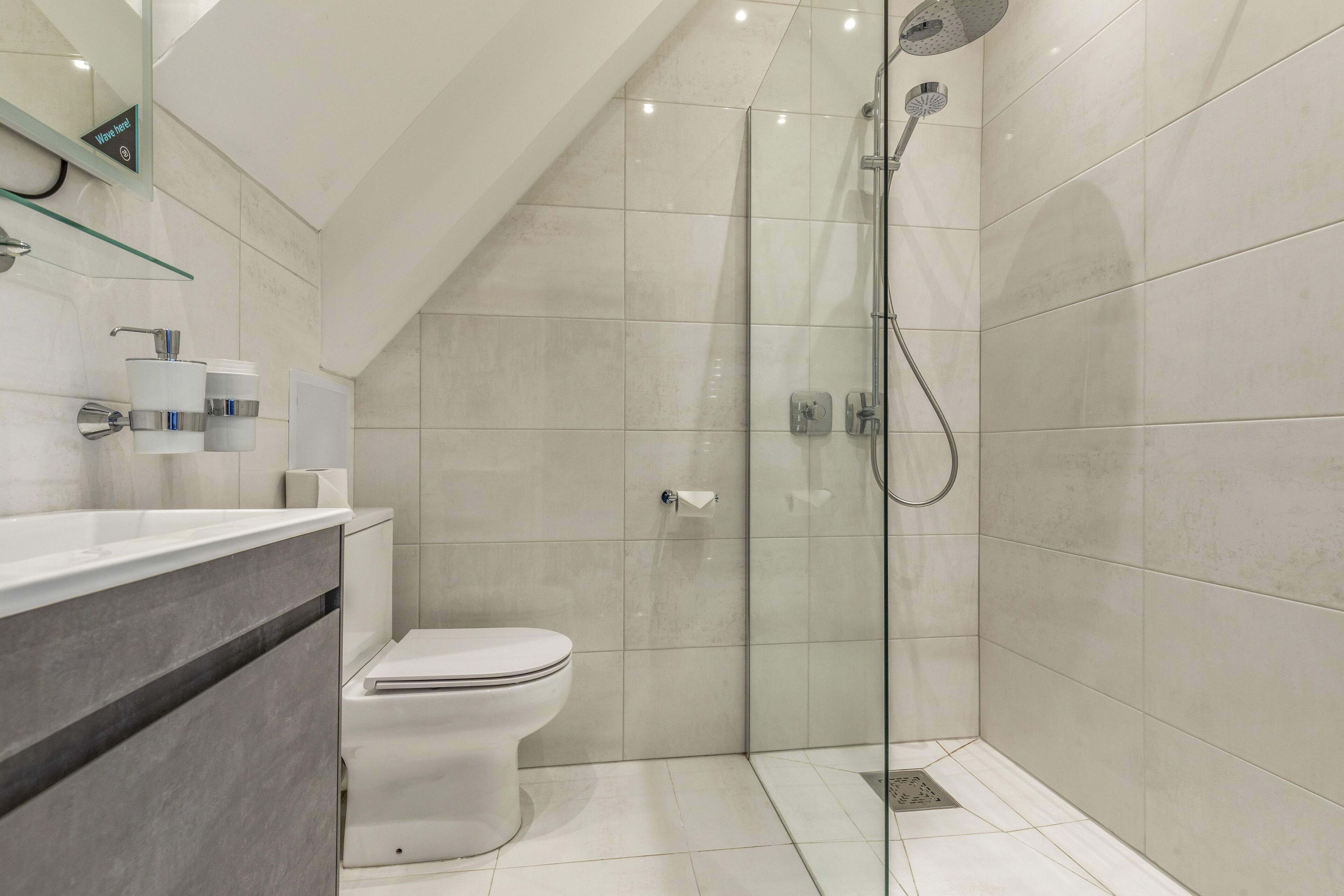 A modern bathroom with a glass-enclosed shower, a toilet, and a vanity with a mirror and towel dispensers.