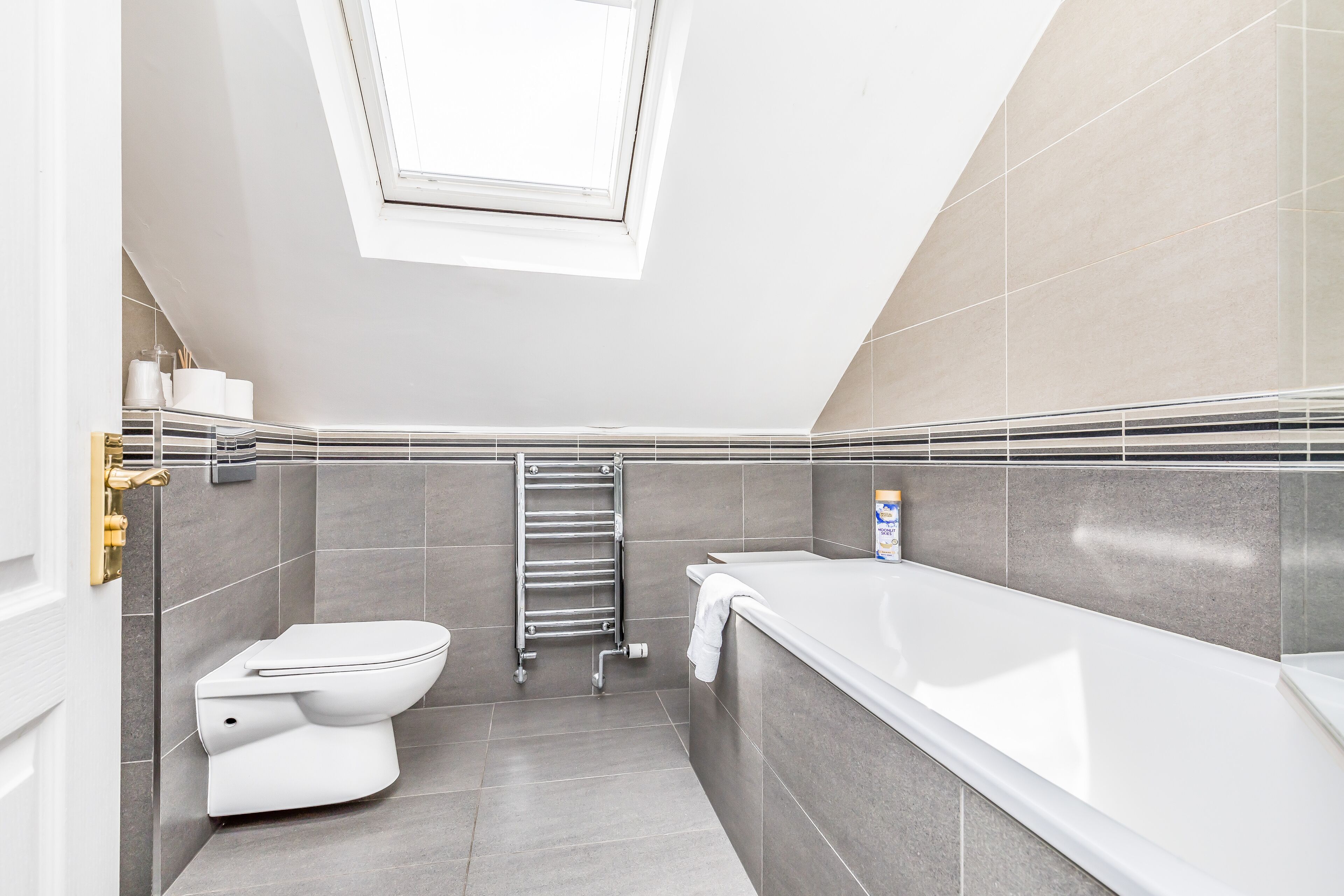 Une salle de bain moderne dotée d’une lucarne, de toilettes, d’une baignoire et d’un porte-serviettes.