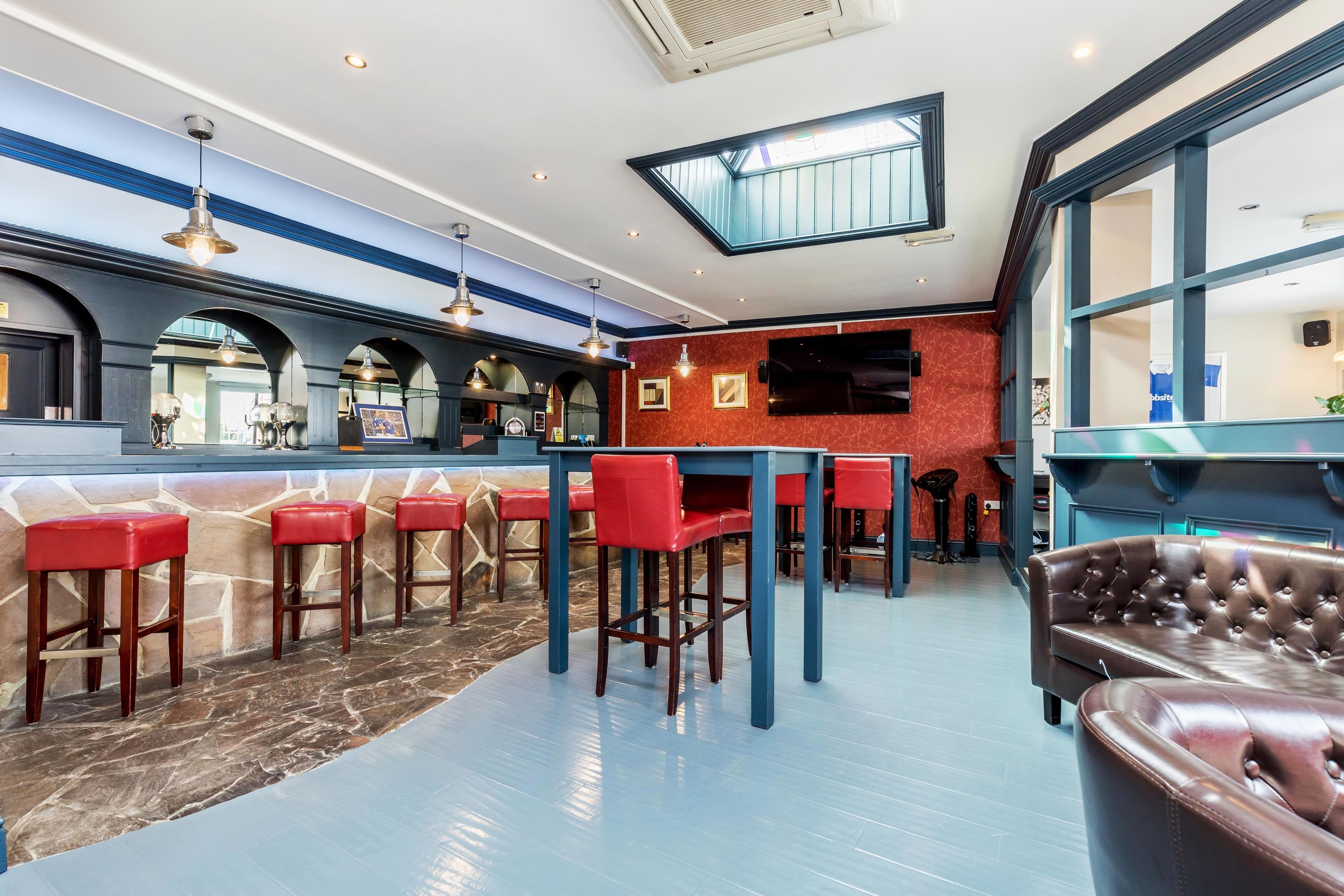 Zona de bar con taburetes rojos, una mesa azul y un sofá de cuero marrón.